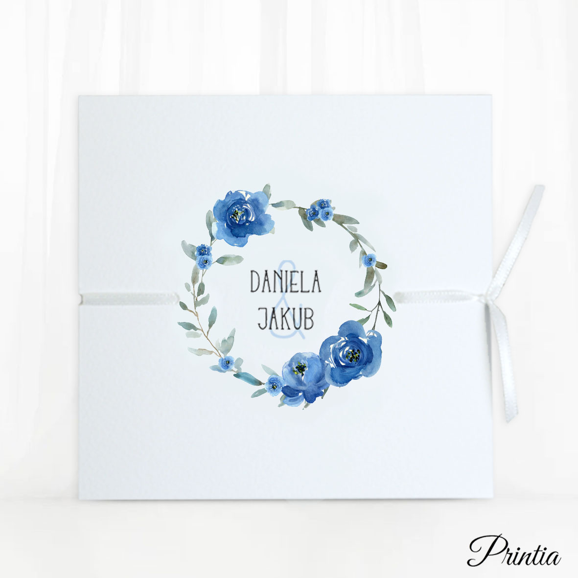 Otevírací svatební oznámení s modrým květinovým kruhem a stuhou